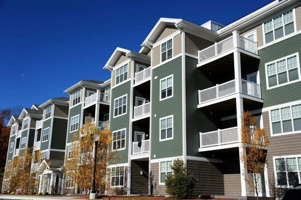 Modern multi-story apartment building with balconies under a clear blue sky.