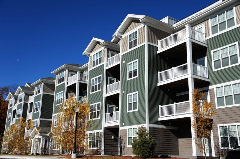 Modern multi-story apartment building with balconies under a clear blue sky.